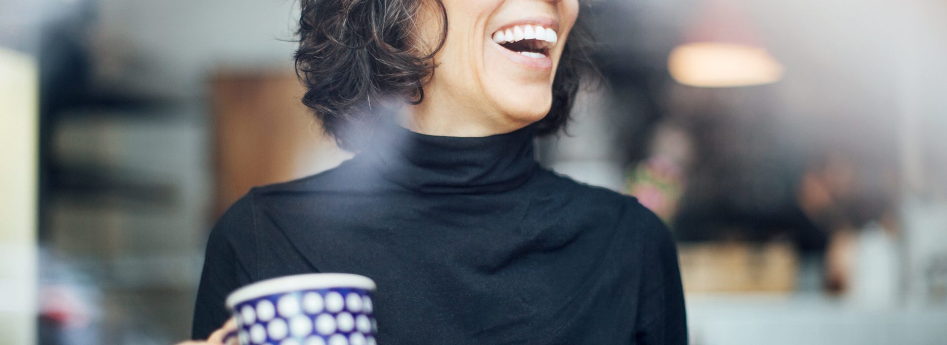 Une femme a grand sourire portant des lunettes et tenant une tasse