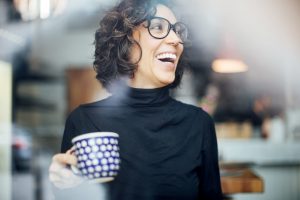 Une femme a grand sourire portant des lunettes et tenant une tasse