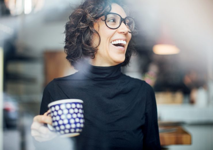 Une femme a grand sourire portant des lunettes et tenant une tasse - axa mobility + retraite