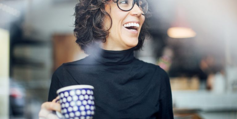 Une femme a grand sourire portant des lunettes et tenant une tasse