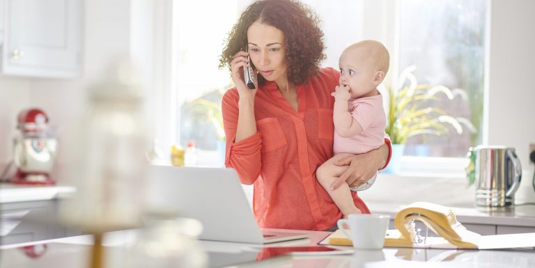 Une femme au téléphone devant son ordinateur et tenant son bébé dans les bras