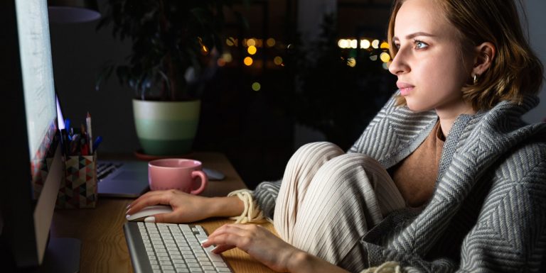 Une femme portant un plaid devant son ordinateur la nuit s'informant sur la maladie de l'endométriose