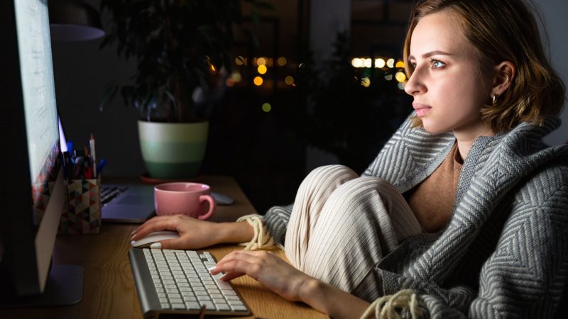Une femme portant un plaid devant son ordinateur la nuit s'informant sur la maladie de l'endométriose
