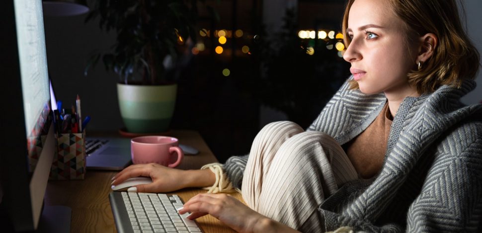 Une femme portant un plaid devant son ordinateur la nuit s'informant sur la maladie de l'endométriose