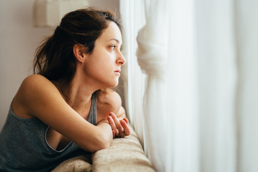 Une femme souffrant d'endométriose regardant par la fenêtre dans son canapé