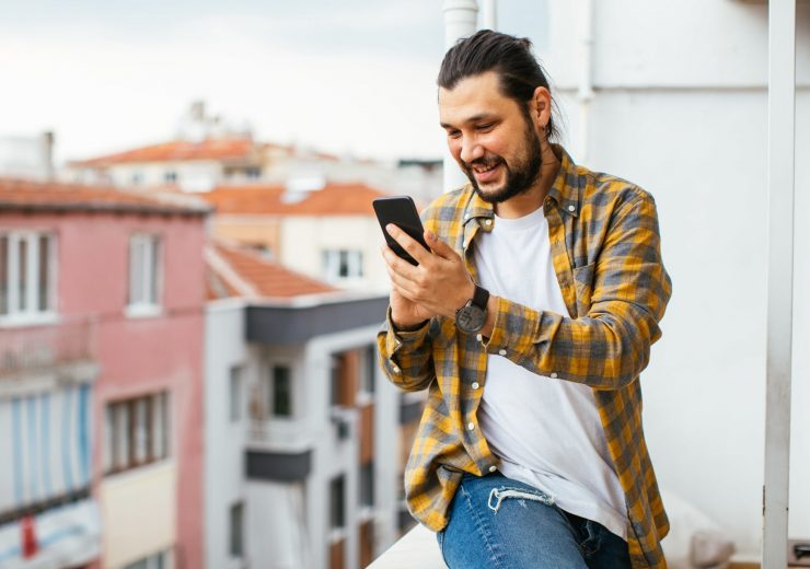 Un homme sur son balcon avec son téléphone dans la main sur l'application AXA épargne salariale