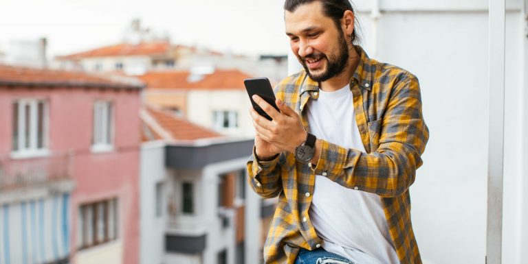 Un homme sur son balcon avec son téléphone dans la main sur l'application AXA épargne salariale