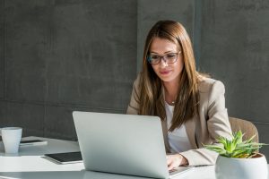 Une femme portant des lunettes au bureau devant son ordinateur sur son espace client entreprise épargne retraite