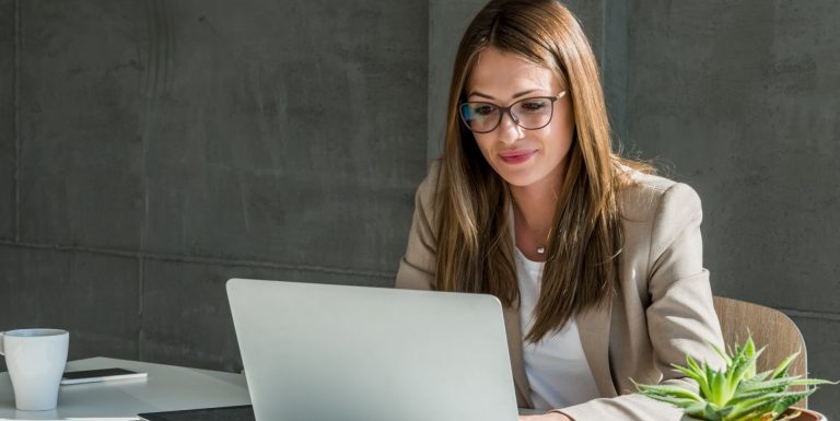 Une femme portant des lunettes au bureau devant son ordinateur sur son espace client entreprise épargne retraite