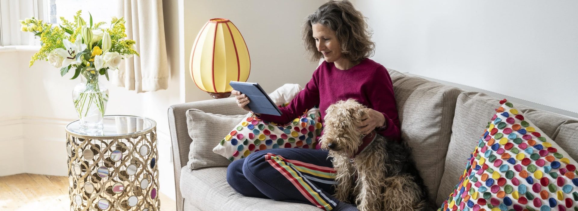 Une femme avec son chien dans son canapé utilisant sa tablette pour simuler des versements volontaires