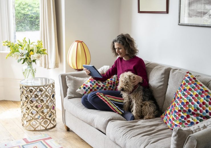 Une femme avec son chien dans son canapé utilisant sa tablette pour simuler des versements volontaires