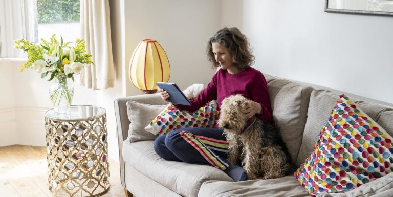 Une femme avec son chien dans son canapé utilisant sa tablette pour simuler des versements volontaires