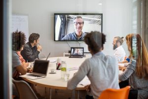 Des hommes et des femmes en réunion d'équipe avec un homme en visioconférence pour discuter de la FAQ Covid-19