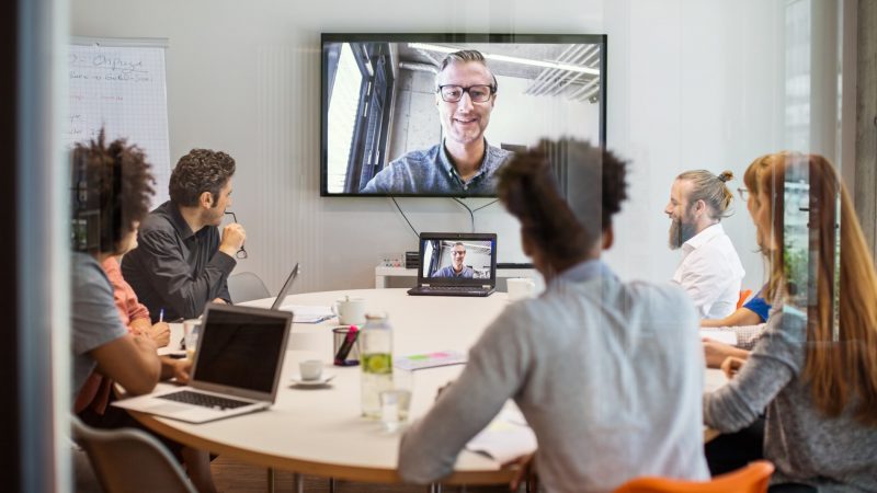 Des hommes et des femmes en réunion d'équipe avec un homme en visioconférence pour discuter de la FAQ Covid-19