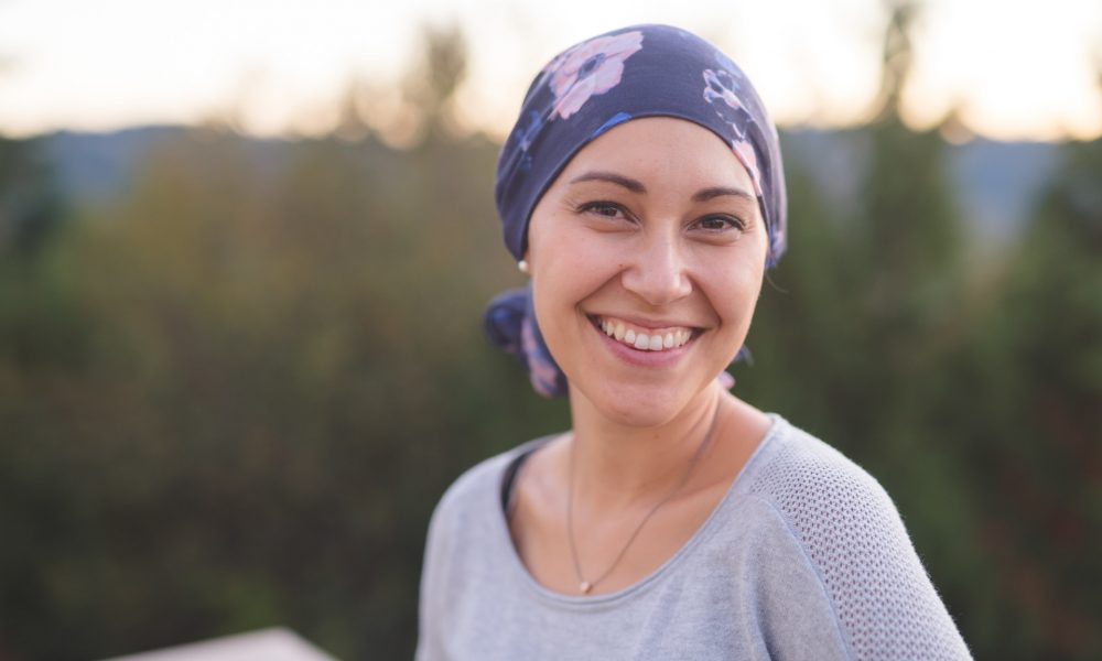 Une femme atteinte d'un cancer avec un bandana sur la tête regardant l'objectif en souriant - soutien maladies graves