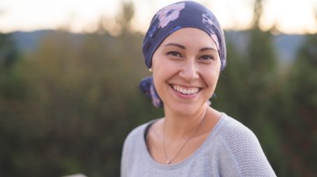 Une femme atteinte d'un cancer avec un bandana sur la tête regardant l'objectif en souriant - soutien maladies graves