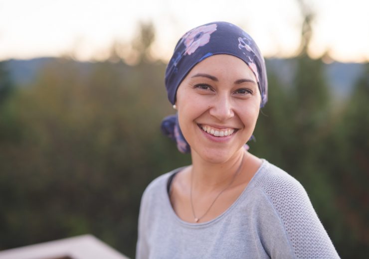 Une femme atteinte d'un cancer avec un bandana sur la tête regardant l'objectif en souriant - bienveillance maladies graves