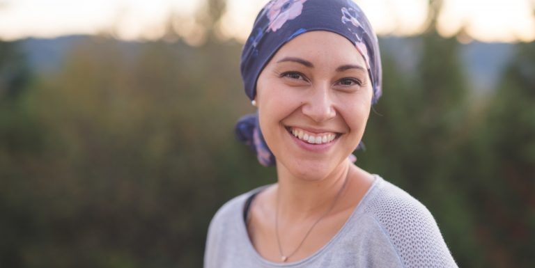 Une femme atteinte d'un cancer avec un bandana sur la tête regardant l'objectif en souriant - soutien maladies graves