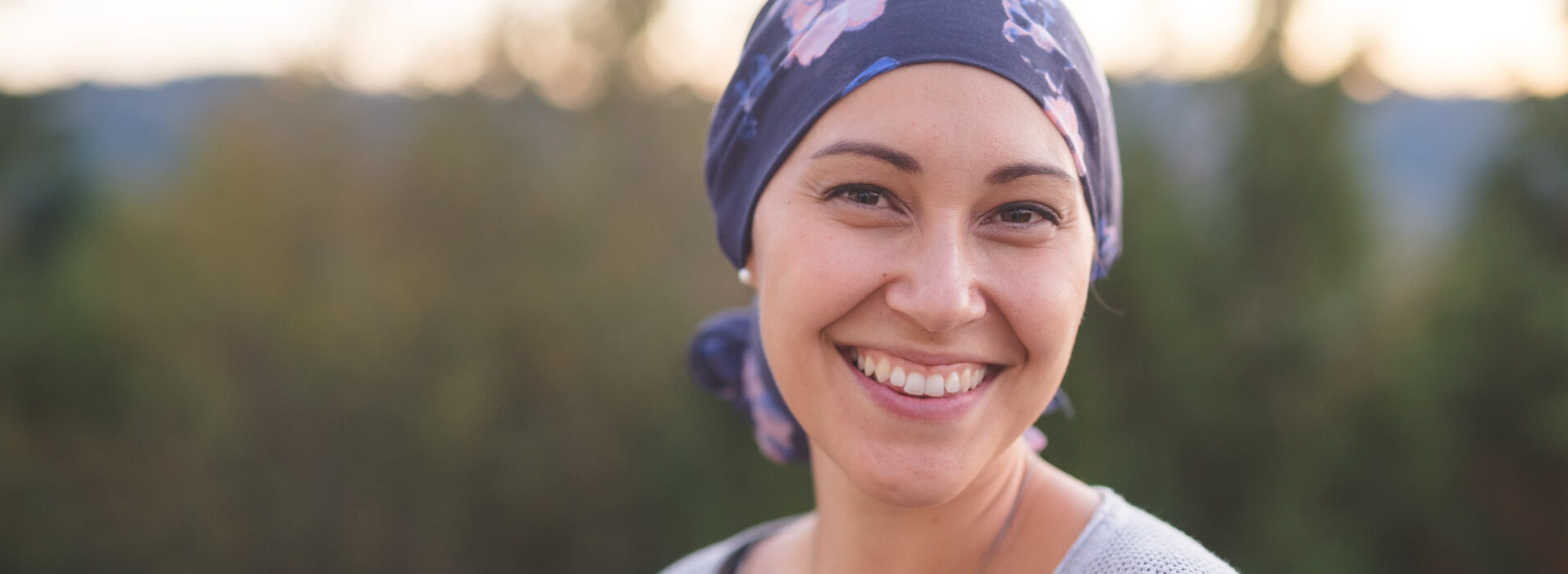 Une femme atteinte d'un cancer avec un bandana sur la tête regardant l'objectif en souriant - bienveillance maladies graves