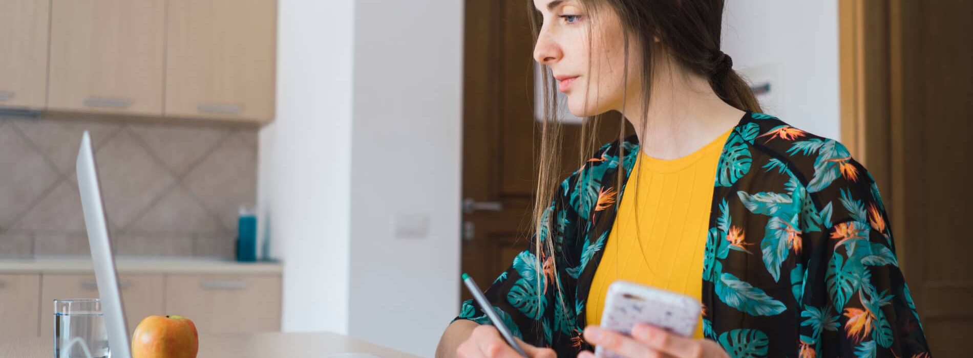 Une femme regarde son ordinateur et prend des notes sur un cahier