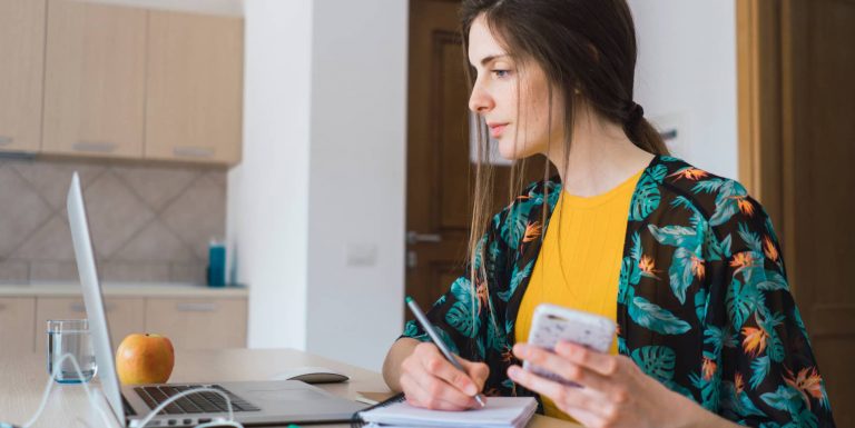 Une femme regarde son ordinateur et prend des notes sur un cahier