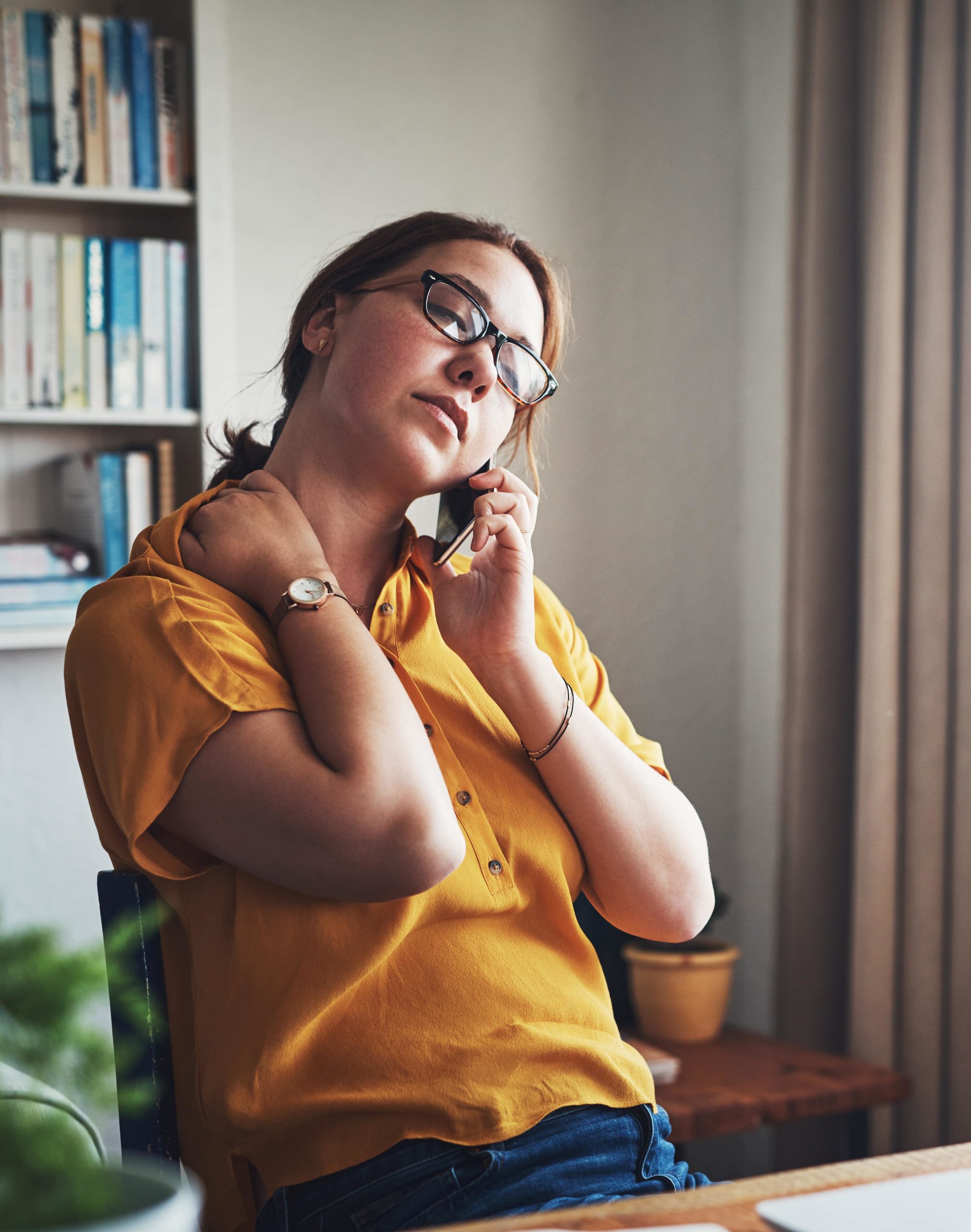 Une femme assise à son bureau au téléphone les yeux fermés se massant la nuque - absentéisme