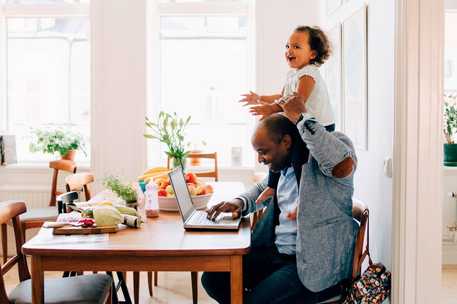 Un père assis devant son ordinateur avec sa petite fille sur les épaules