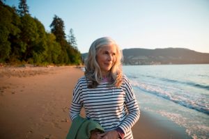 Une femme senior se baladant seule sur une plage au couché du soleil