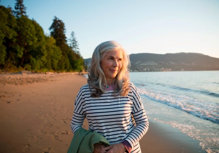 Une femme senior se baladant seule sur une plage au couché du soleil