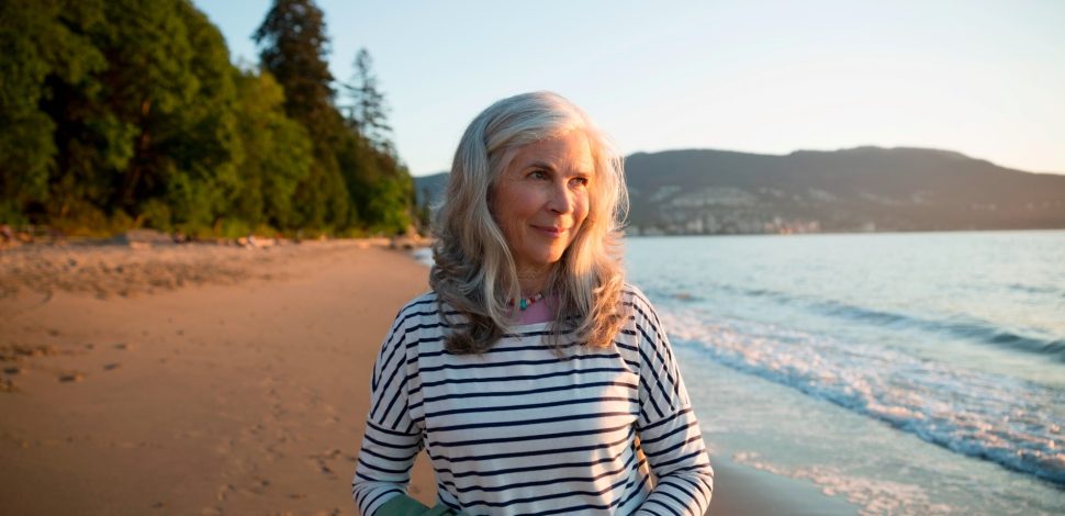 Une femme senior se baladant seule sur une plage au couché du soleil