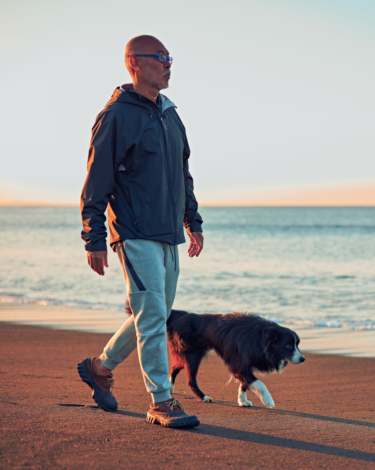 Un homme marchant avec son chien sur un plage au soleil couchant – santé mentale