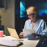 Une femme avec sa fiche de paie dans les mains regardant son ordinateur - Montant net social