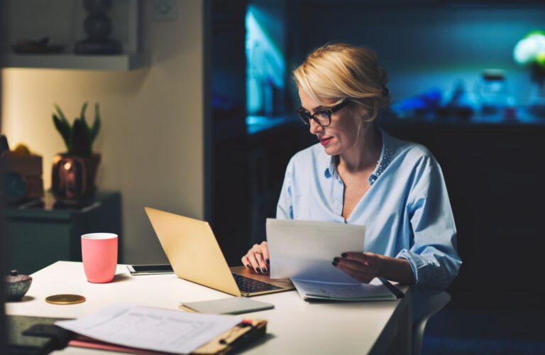 Une femme avec sa fiche de paie dans les mains regardant son ordinateur - Montant net social