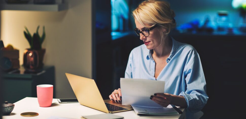 Une femme avec sa fiche de paie dans les mains regardant son ordinateur - Montant net social