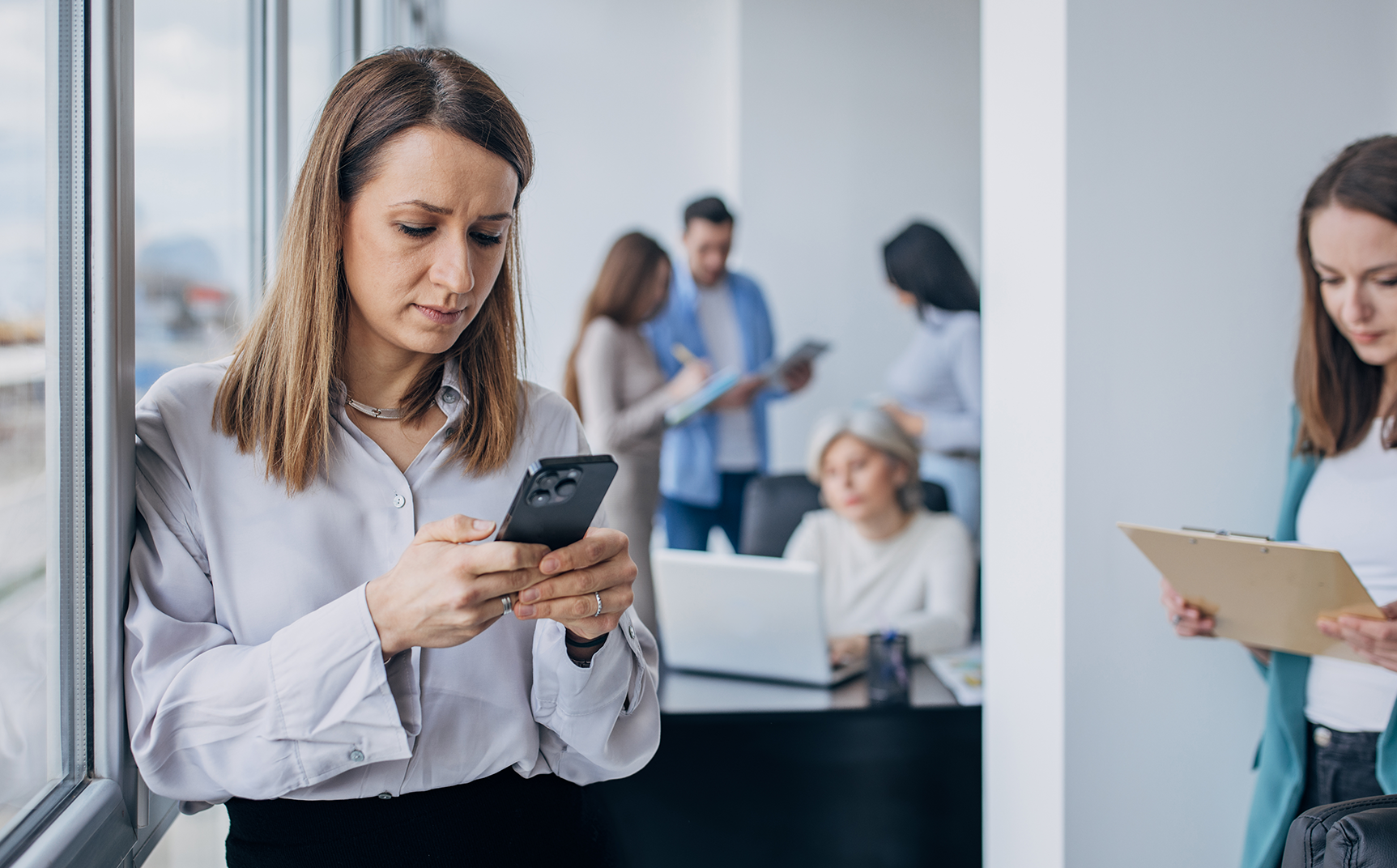 Une femme observe son téléphone dans un environnement de travail - Violences Conjugales
